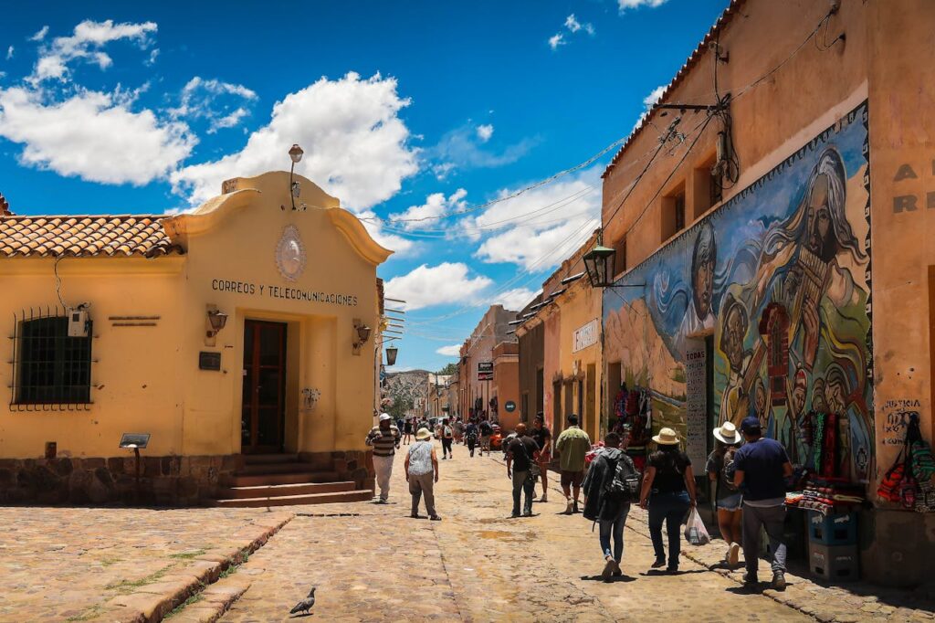 Vibrant street scene in a historic town with locals and tourists walking by colorful murals.